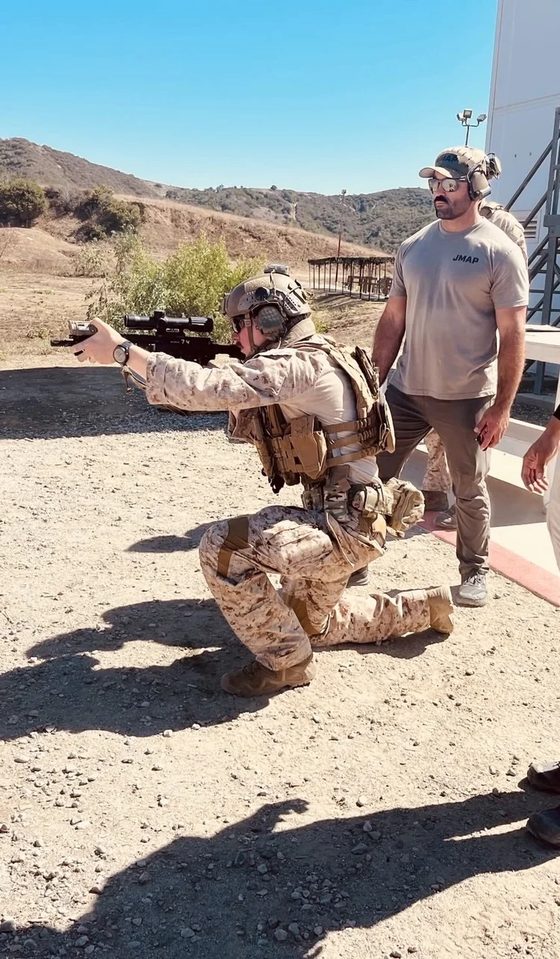 Erik Small kneeling and firing a pistol while an instructor stands behind