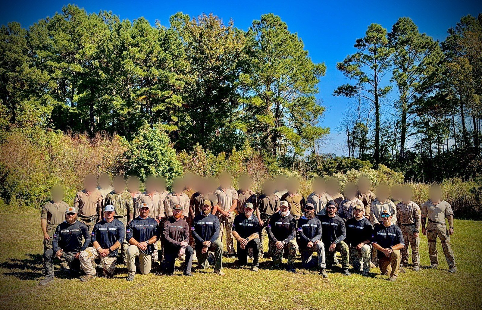Scoring Tech instructors in PROCESS > OUTCOME shirts kneeling in front of a class of operators; faces of the class blurred